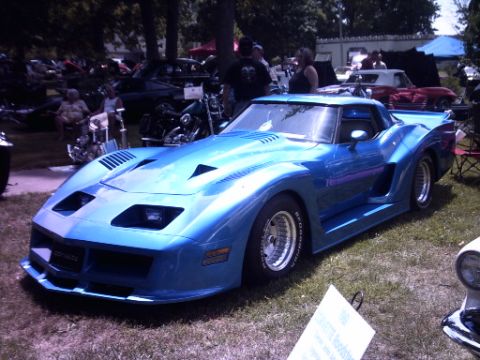 1995 Ford Probe - A modified blue sports car, possibly a Corvette, is displayed outdoors among other vehicles and people.