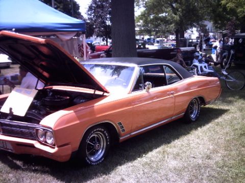 1995 Ford Probe - A vintage orange coupe with its hood raised is displayed outdoors on a sunny day.