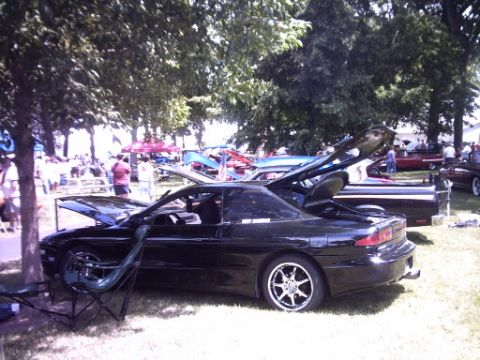 1995 Ford Probe - A black coupe with its hoods open sits on display at an outdoor car show with other vehicles and people around.