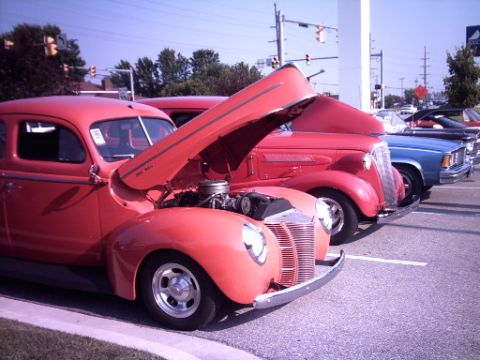 1995 Ford Probe - A row of cars are parked at a car show, with the hood of a red vintage vehicle open to display its engine.