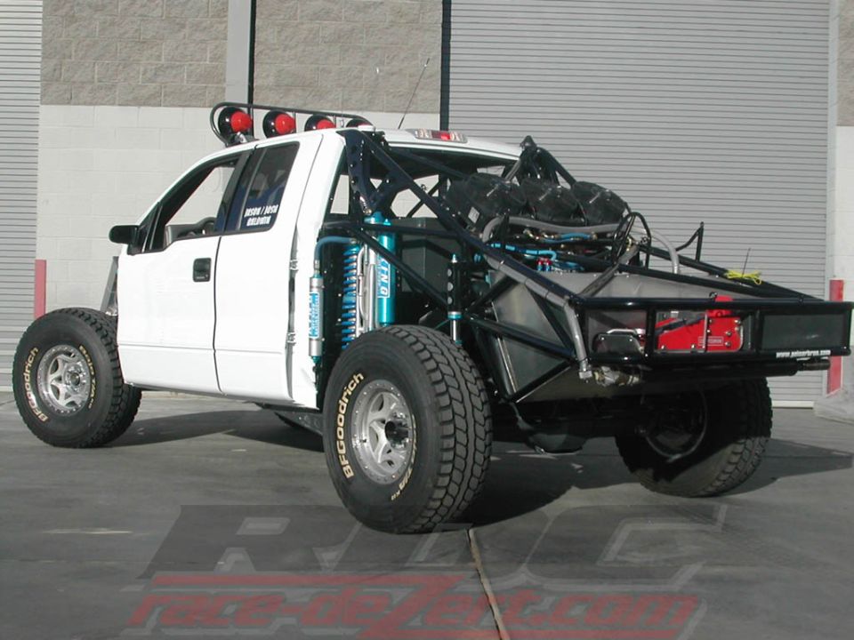 White custom off-road truck with roll cage and large tires. Some text visible on door
