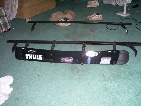 1991 Ford Bronco - A Thule snowboard carrier and roof rack are laid out on a carpeted floor, with various stickers adorning the carrier.