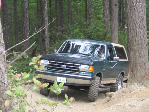1990 Ford Bronco - This Ford Bronco navigates a wooded trail with its tires on uneven terrain.