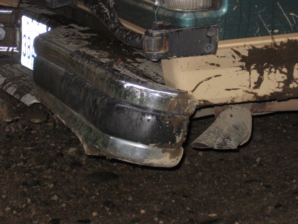 Muddy chrome rear bumper and frame of a truck with a fallen mud flap, shot at night
