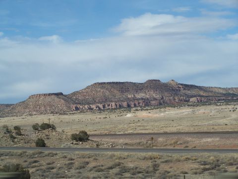 1995 Ford Probe - A vast desert landscape unfolds with layered mesas under a dramatic sky, with a road cutting through the terrain.