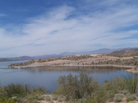 1995 Ford Probe - A scenic view of a desert lake with many cars parked along the shoreline under a partly cloudy sky.
