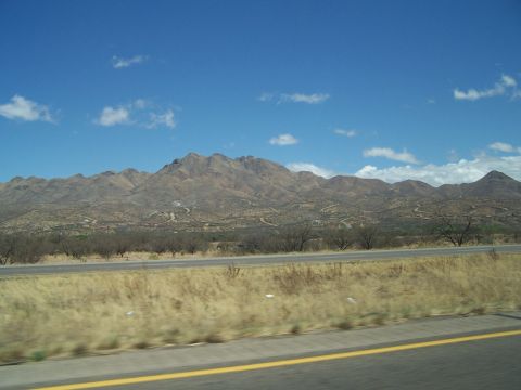 1995 Ford Probe - A wide view of a desert highway stretching towards distant mountains under a bright, cloudy sky.