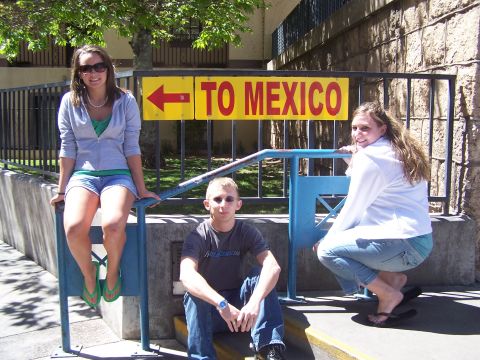 1995 Ford Probe - A group of friends takes a photo at a border crossing sign, with one person sitting on a railing and two others on steps.
