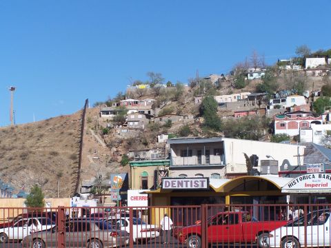 1995 Ford Probe - A border wall divides a hillside town, with businesses and vehicles visible below.
