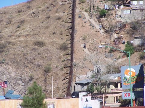 1995 Ford Probe - A view of a border fence on a dry, rocky hillside with scattered buildings and a street lamp.