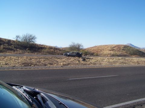 1995 Ford Probe - A dark car with a spoiler sits on the shoulder of a highway under a clear blue sky.
