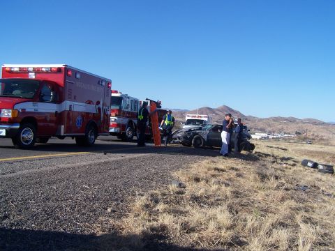 1995 Ford Probe - Emergency responders at the scene of a car accident on a sunny day with mountains in the background.