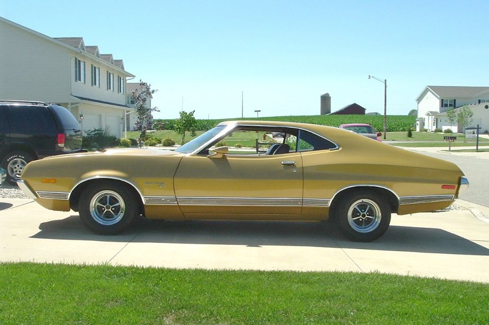 Gold 1970s Ford Gran Torino fastback parked in a driveway in a suburban neighborhood