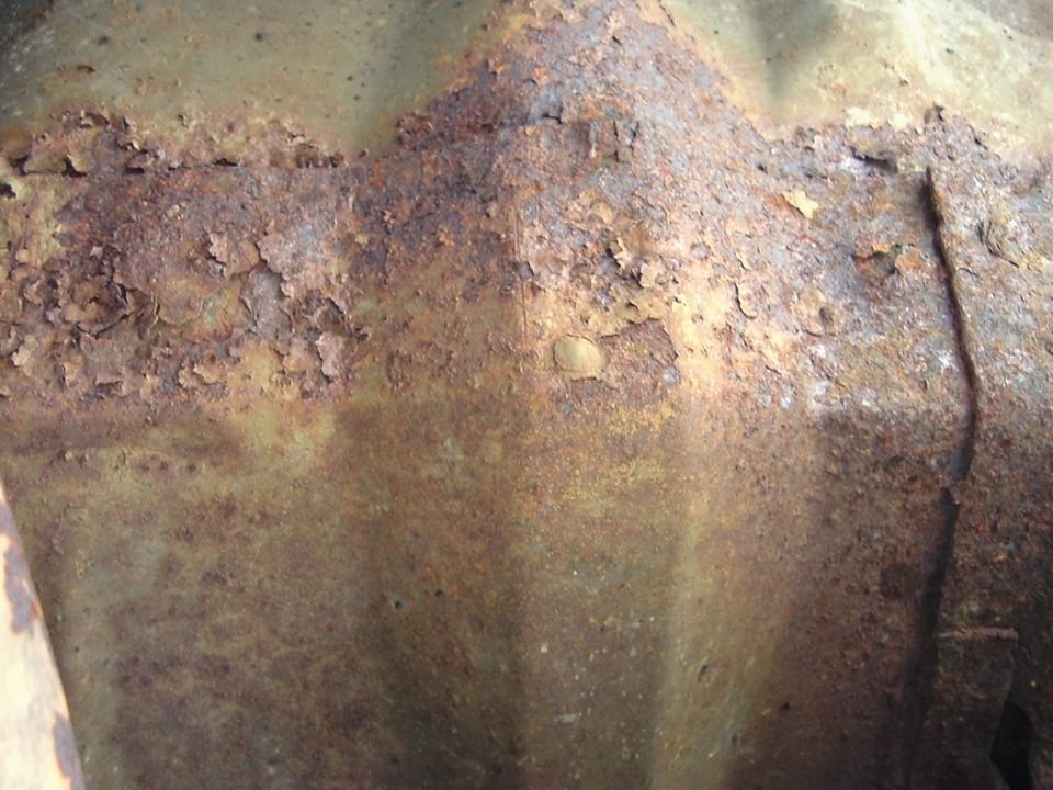 Heavily rusted and pitted sheet metal panel with flaking surface corrosion and a crease line