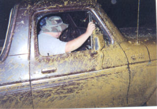 1979 Ford Bronco - A person sits in the driver's seat of a heavily mud-covered vehicle, obscuring most details.