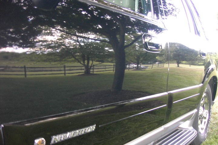 Black SUV side panel with chrome trim and 'Navigator' badge reflecting a grassy fenced field