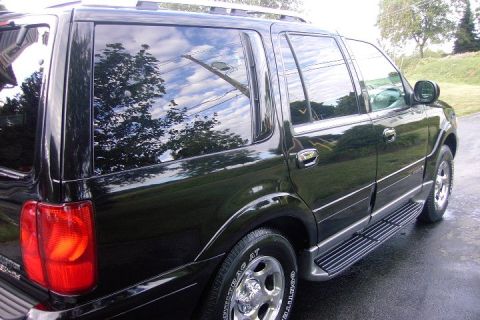 1996 Mercury Grand Marquis - A black SUV is shown from the rear three-quarter angle, reflecting trees and sky in its windows.