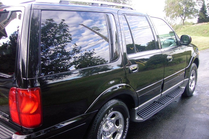 Black full-size SUV, rear three-quarter passenger side view on wet pavement