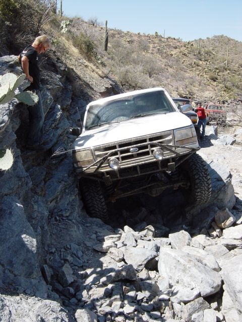 1993 Ford Bronco - A white Ford truck is shown navigating a difficult rocky terrain, with another vehicle visible in the background.