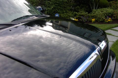1996 Mercury Grand Marquis - Front view of a black car's hood and grille, reflecting the sky and surrounding greenery.