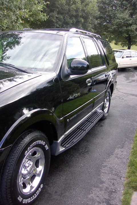 1996 Mercury Grand Marquis - Side view of a black SUV, chrome running boards and tinted windows. Another vehicle is visible in the background.