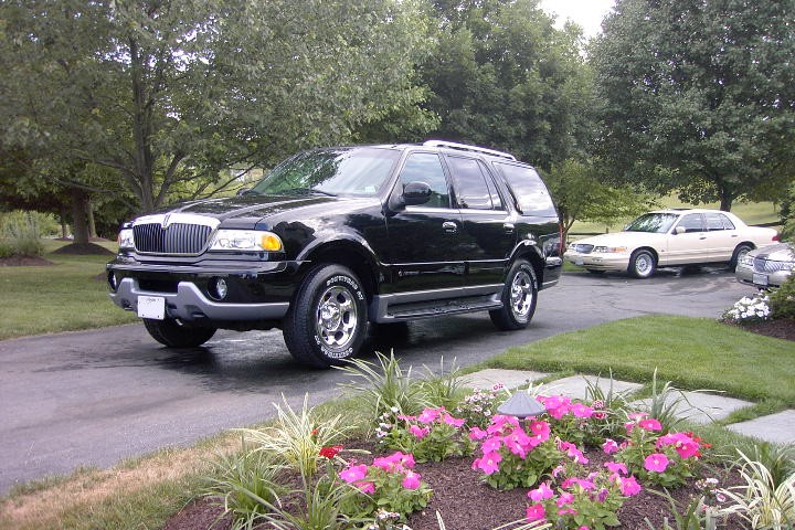 Black Lincoln Navigator parked in a driveway with a gold Mercury Grand Marquis sedan behind it