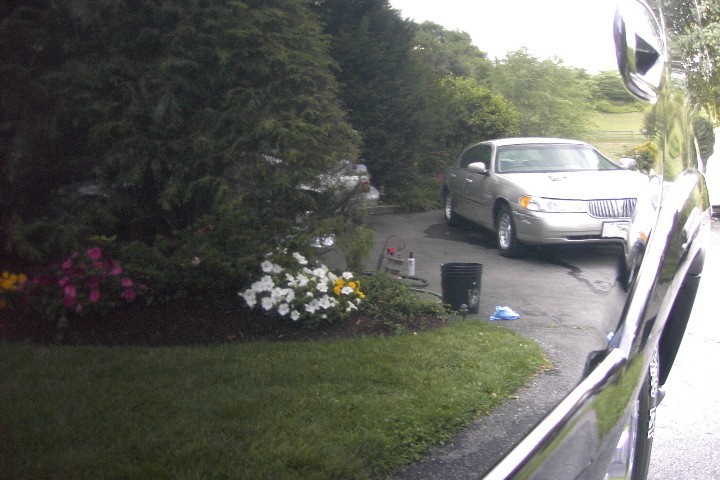 Silver full-size sedan parked on driveway seen past dark car body
