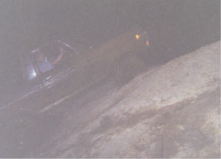 1979 Ford Bronco - A dark-colored Ford Bronco is seen from the side, partially covered by what appears to be dirt or rock.