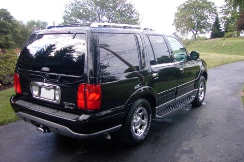 1996 Mercury Grand Marquis - A black SUV is parked on a wet driveway with trees in the background.