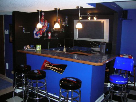 1994 Ford Bronco - A home bar setup features blue cabinetry, Ford-branded stools, and a Budweiser sign on the wall.