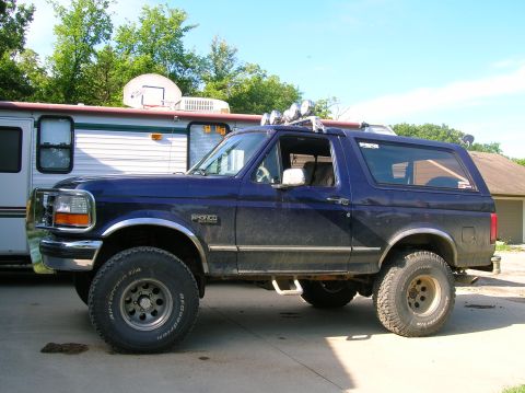 1994 Ford Bronco - A blue Ford Bronco is parked in a driveway next to a recreational vehicle under a clear sky.