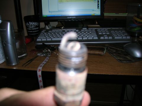 1994 Ford Bronco - A close-up of a spark plug is shown, with a desk and computer setup in the background.