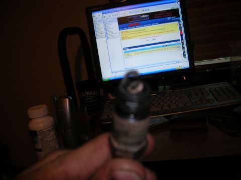 1994 Ford Bronco - A spark plug is shown in focus, with a computer displaying a website in the background.