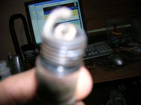 1994 Ford Bronco - Close-up of a spark plug held by a hand, with a computer setup in the background.