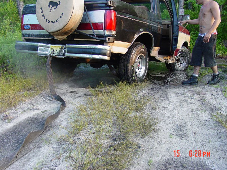 Black and tan Ford Bronco with spare tire on rear, stuck in dirt