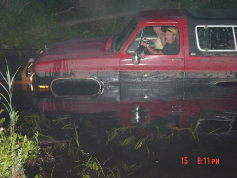 1995 Dodge 1500 - Two people are inside a red and black SUV that is stuck in water with water and vegetation.