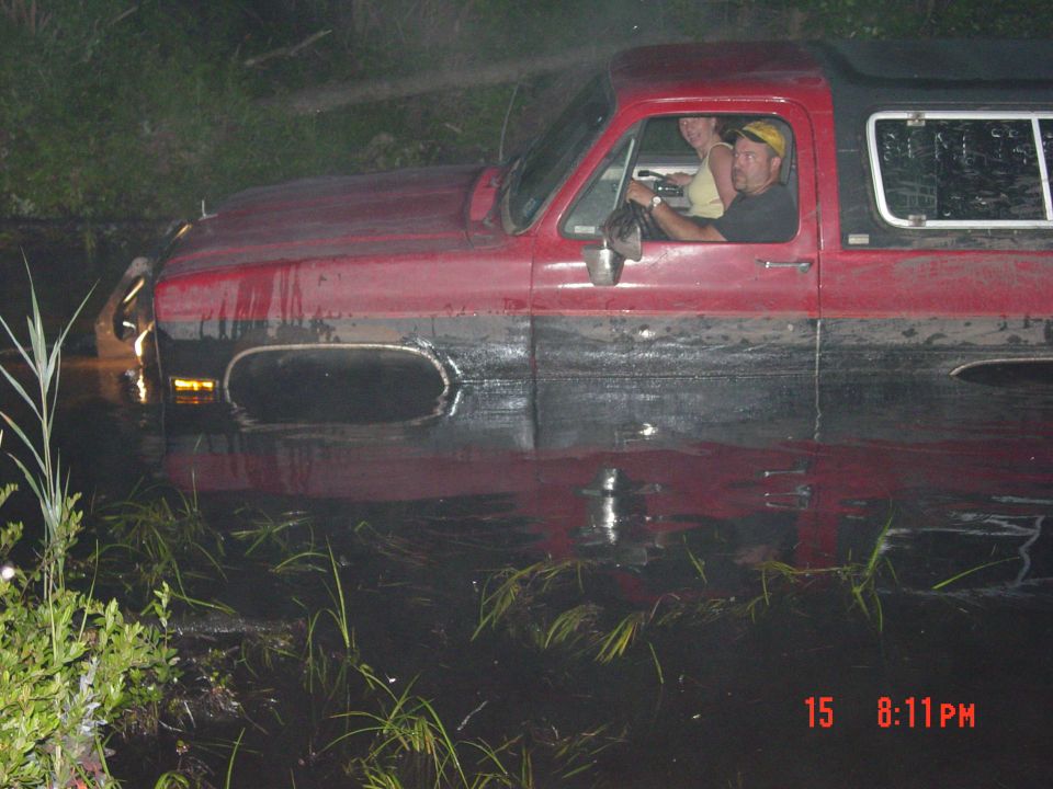 Red and black SUV partially submerged in murky water, with two people inside