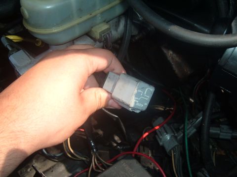 1988 Ford Bronco - A hand holds a gray electrical relay with a wiring diagram visible, positioned near a brake fluid reservoir in an engine bay.