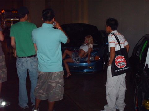 1995 Ford Probe - A woman poses on the hood of a blue 1995 Ford Probe, with onlookers and another vehicle visible.