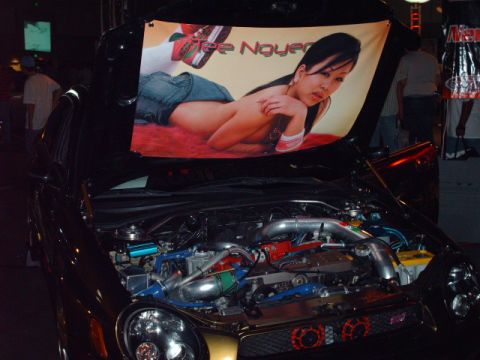 1995 Ford Probe - The hood is open revealing a modified engine bay and a banner a woman with the name 'Tee Noyer'.