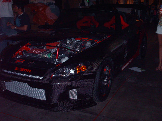 Black Honda S2000 with red interior and exposed engine bay. Carbon fiber body kit and aftermarket wheels