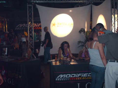 1995 Ford Probe - Event attendees sign autographs at tables with promotional banners and lighting overhead.