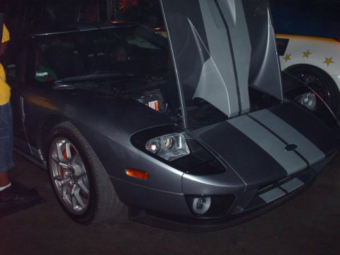 1995 Ford Probe - A dark gray Ford GT with racing stripes has its hood open, parked next to another vehicle.