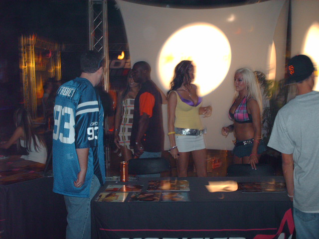 People gathered around tables at an event, some women are standing near a bright light