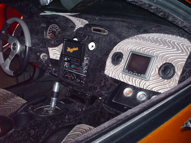 Car interior with fuzzy black dash, aftermarket steering wheel, and two screens. One screen has 'Meguiar's' logo