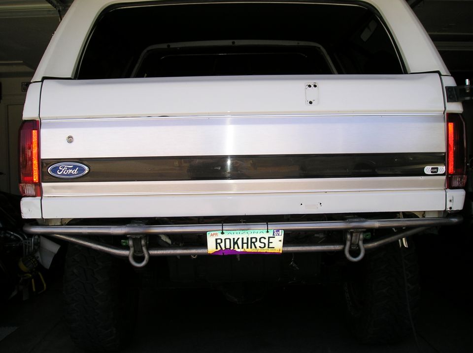 Rear of white Ford Bronco with tubular bumper and Arizona ROKHRSE plate in garage