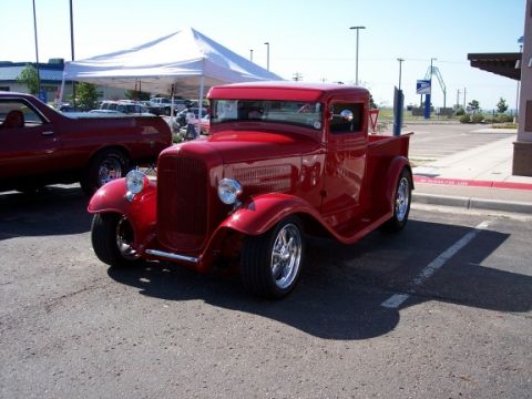 1972 Ford Ranchero - A bright red hot rod pickup truck is parked next to another vehicle under a white tent.