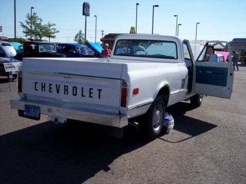 1972 Ford Ranchero - A white Chevrolet pickup truck is parked at an outdoor event with its doors open. Other vehicles are visible in the background.