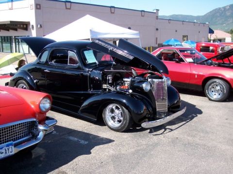 1972 Ford Ranchero - A black coupe is displayed with its hood open, parked next to other vehicles at an outdoor event.