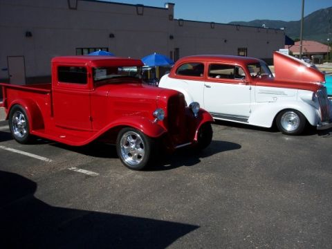 1972 Ford Ranchero - Two classic cars, a red pickup and a two-tone sedan, are parked outside a building on a sunny day.
